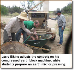 Larry Elkins adjusts the controls on his compressed earth block machine, while students prepare an earth mix for pressing.